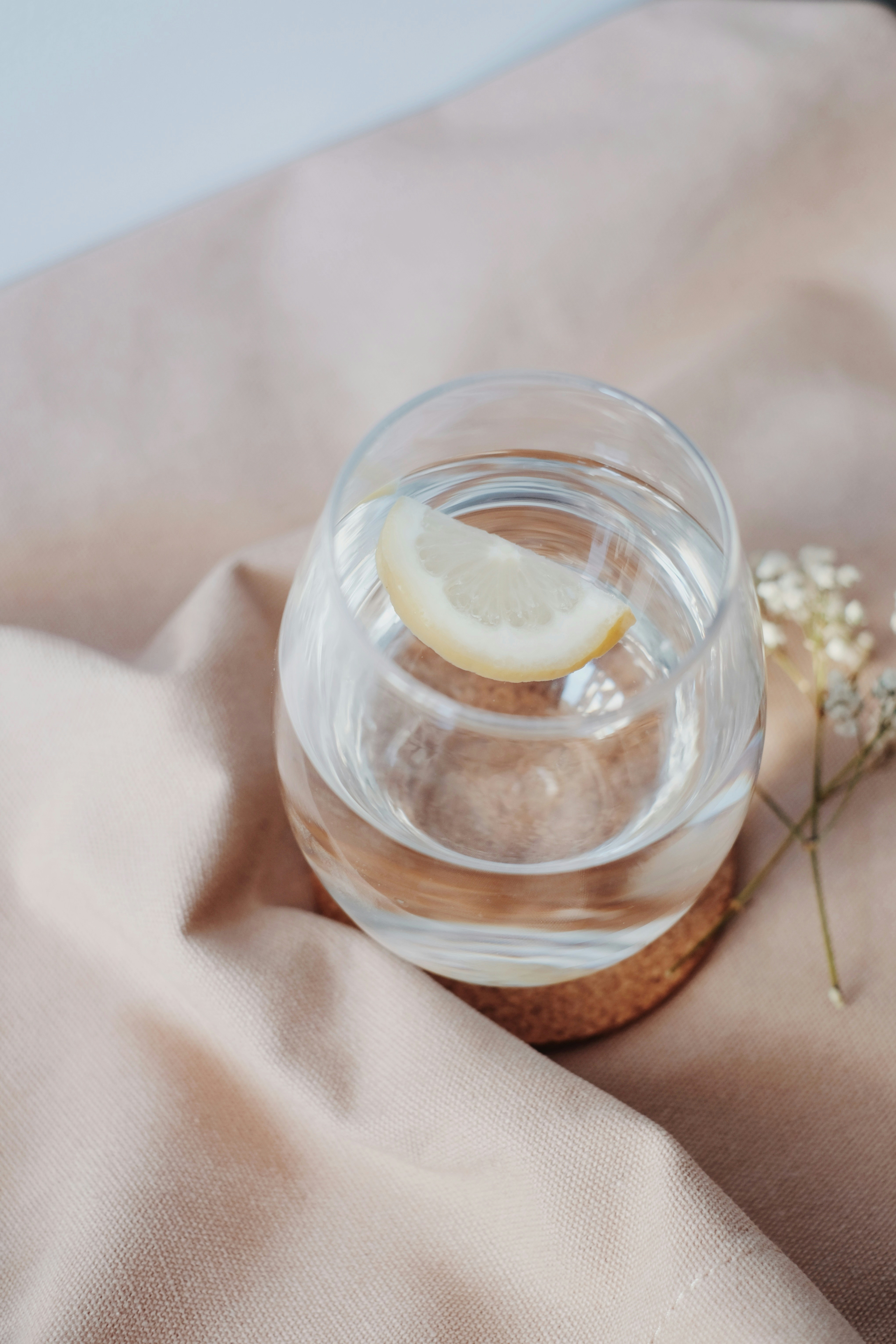 A glass of water with a slice of lemon resting on a cork coaster